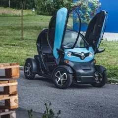 Niebiesko-czarny Renault Twizy z otwartymi drzwiami, obok drewnianych palet. Sprawdź, jaka jest renault twizy cena!