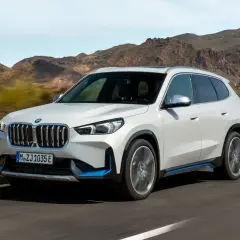 Biały ix1 BMW z niebieskimi akcentami jedzie po drodze, w tle góry.