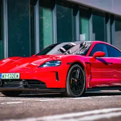 Czerwony Porsche Taycan Turbo z czarnymi felgami stoi przed nowoczesnym budynkiem.