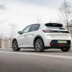 Biały Peugeot e-208 z zieloną tablicą rejestracyjną WE 5G959 zaparkowany na drodze.