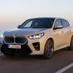 Nowy, beżowy BMW iX2 jedzie wzdłuż wybrzeża.