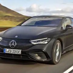 Elegancki, czarny Mercedes EQE sunie po drodze wśród malowniczych wzgórz.