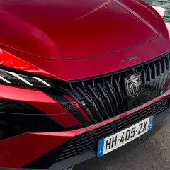 Czerwony Peugeot 408 Hybrid z charakterystycznym grillem i ostrymi światłami LED, gotowy do podróży nad wodę.