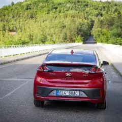 Czerwony Hyundai Ioniq Hybrid na moście, otoczony zielonymi wzgórzami.