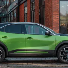 Zielony Opel Mokka Electric z czarnym dachem stoi przed sklepem.