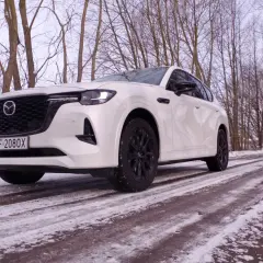 Biała Mazda hybryda na ośnieżonej drodze, otoczona zimowym lasem.