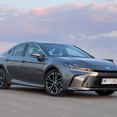 Szary Toyota Camry 2.5 Hybrid na tle zachodzącego słońca i domów.