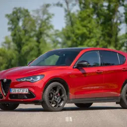 Czerwone Alfa Romeo Stelvio na drodze, z zielenią w tle. Zastanawiasz się nad jego spalaniem?