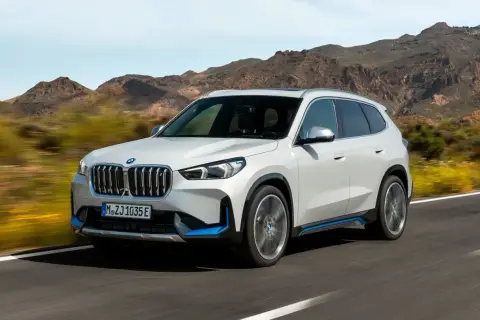 Biały ix1 BMW z niebieskimi akcentami jedzie po drodze, w tle góry.