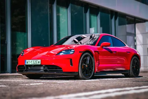 Czerwony Porsche Taycan Turbo z czarnymi felgami stoi przed nowoczesnym budynkiem.