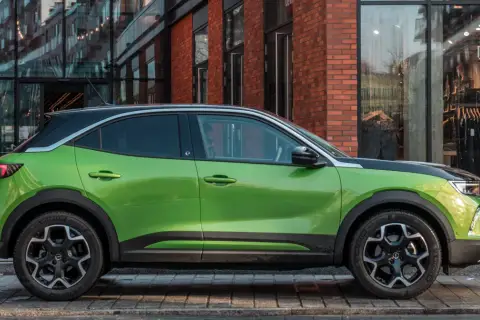 Zielony Opel Mokka Electric z czarnym dachem stoi przed sklepem.