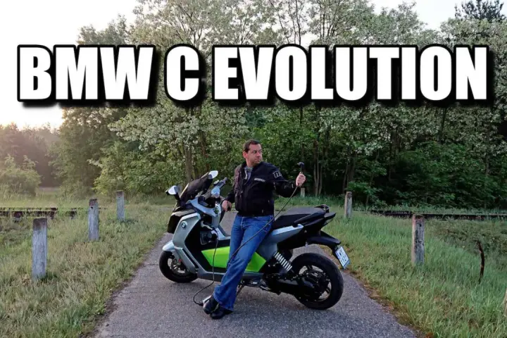 Mężczyzna siedzi na skuterze BMW C Evolution, podłączonym do ładowania. Tło to malowniczy krajobraz z drzewami.