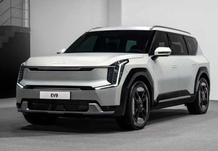 Biały, futurystyczny SUV Kia EV9 z charakterystycznymi światłami LED i masywnymi felgami stoi na szarym tle.