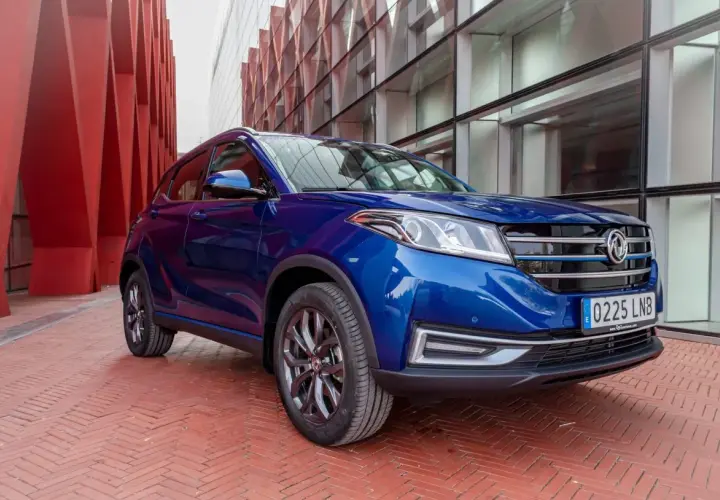 Niebieski SUV DFSK Seres 3 na tle nowoczesnej architektury.