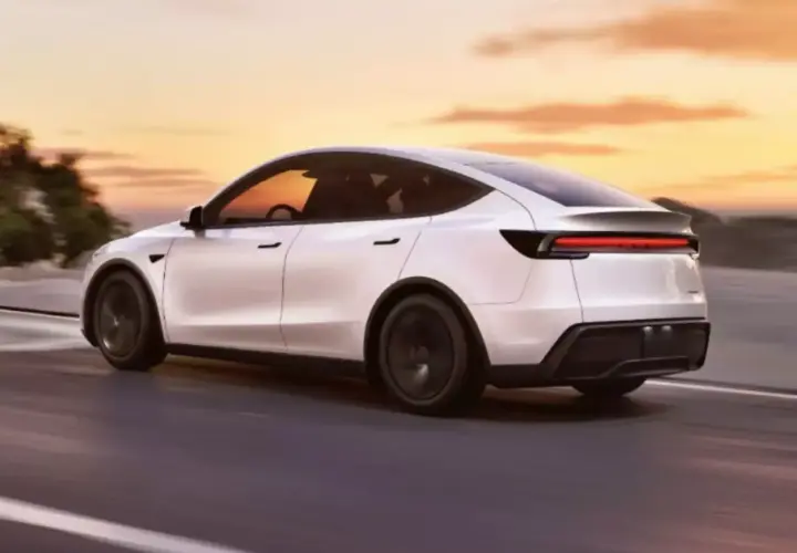 Biały Tesla Y 2025 pędzi po drodze o zachodzie słońca.