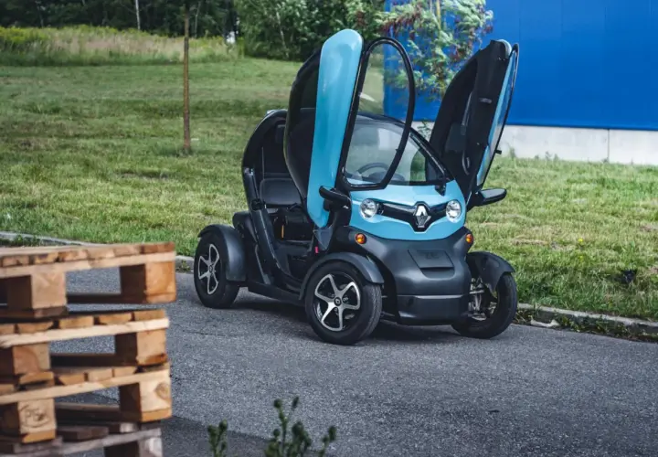 Niebiesko-czarny Renault Twizy z otwartymi drzwiami, obok drewnianych palet. Sprawdź, jaka jest renault twizy cena!
