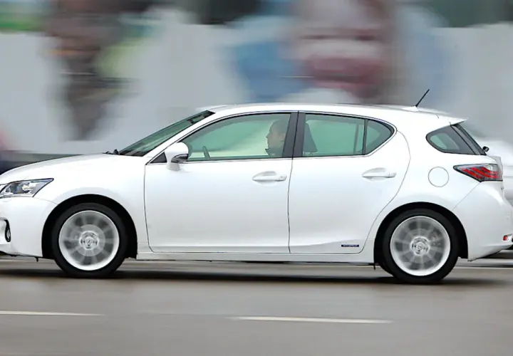 Biały Lexus CT200h w ruchu ulicznym, z rozmytym tłem i innymi samochodami.