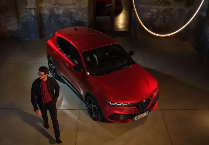 Elegancki mężczyzna obok czerwonego Alfa Romeo Tonale. Sprawdź aktualną alfa romeo tonale cena i odkryj jego styl.