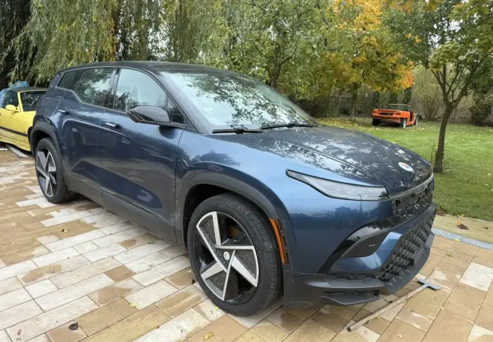 Nowy, granatowy Fisker SUV stoi na wybrukowanym podjeździe. W tle żółty i pomarańczowy samochód.