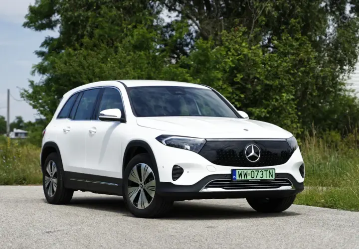 Biały Mercedes EQB na tle zieleni i nieba. Elektryczny SUV z charakterystycznym grillem i nowoczesnymi światłami.