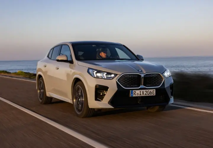 Beżowe BMW iX2 jedzie wzdłuż wybrzeża.