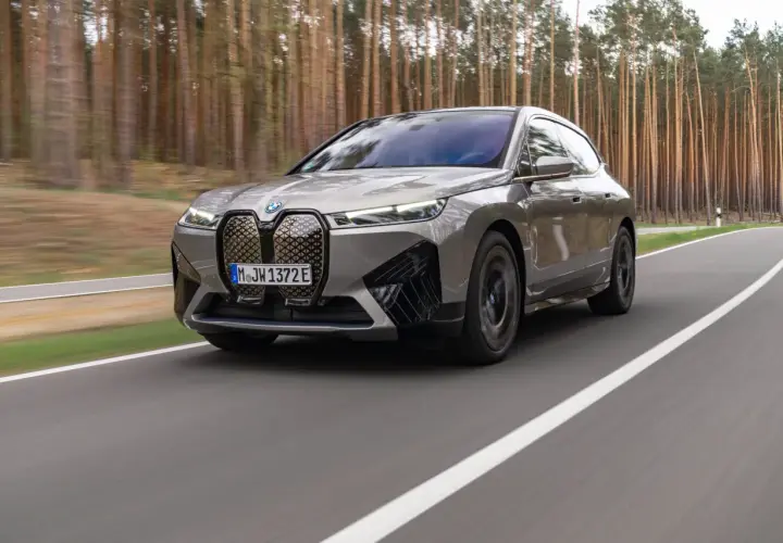 Szary BMW iX jedzie po drodze wśród drzew.