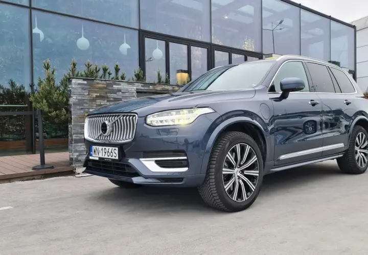 Elegancki, ciemnoszary Volvo XC90 T8 z nowoczesnymi światłami LED stoi przed budynkiem z dużymi, przeszklonymi oknami.