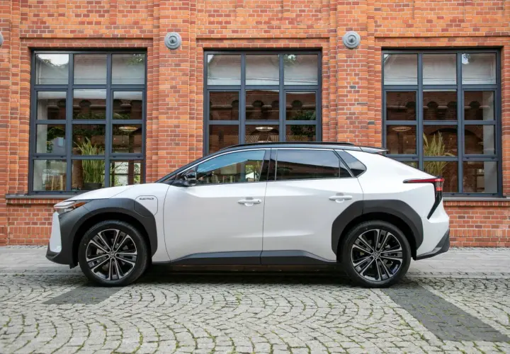 Biały Toyota bZ4X elektryczny SUV stoi na brukowanej ulicy przed ceglanym budynkiem z dużymi oknami.