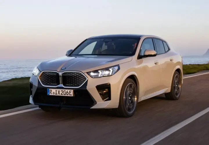 Nowy, beżowy BMW iX2 jedzie wzdłuż wybrzeża.