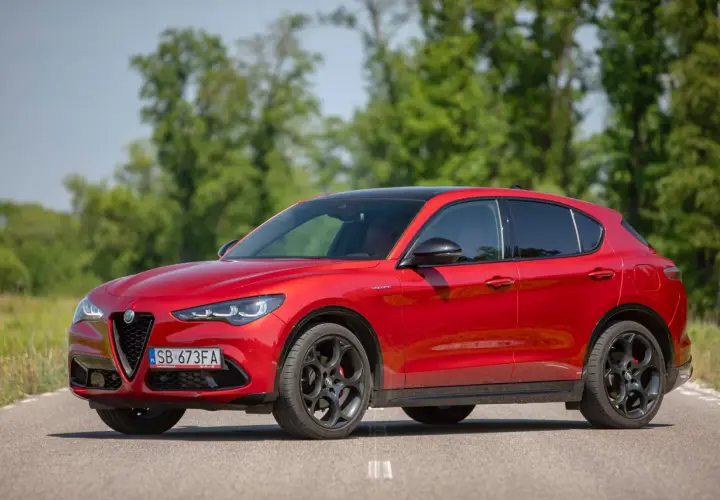 Czerwone Alfa Romeo Stelvio na drodze, z zielenią w tle. Zastanawiasz się nad jego spalaniem?