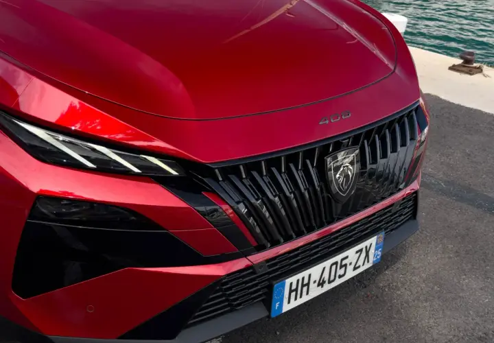 Czerwony Peugeot 408 Hybrid z charakterystycznym grillem i ostrymi światłami LED, gotowy do podróży nad wodę.