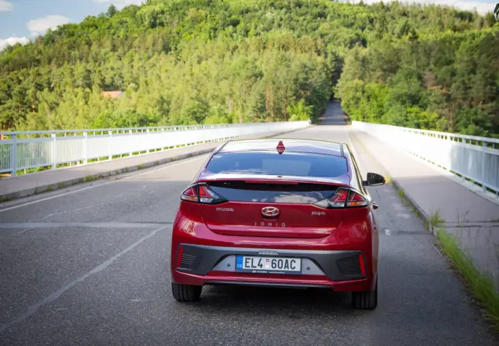 Czerwony Hyundai Ioniq Hybrid na moście, otoczony zielonymi wzgórzami.
