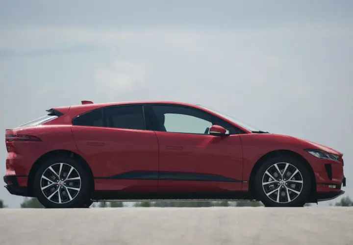 Czerwony jaguar elektryczny z profilu, z widocznymi felgami i linią dachu.