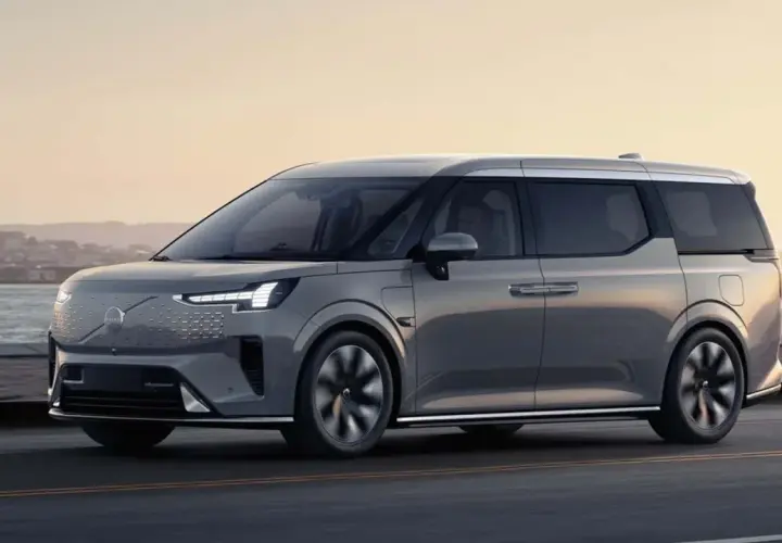 Szary Volvo EM90 jedzie wzdłuż wybrzeża o zachodzie słońca.