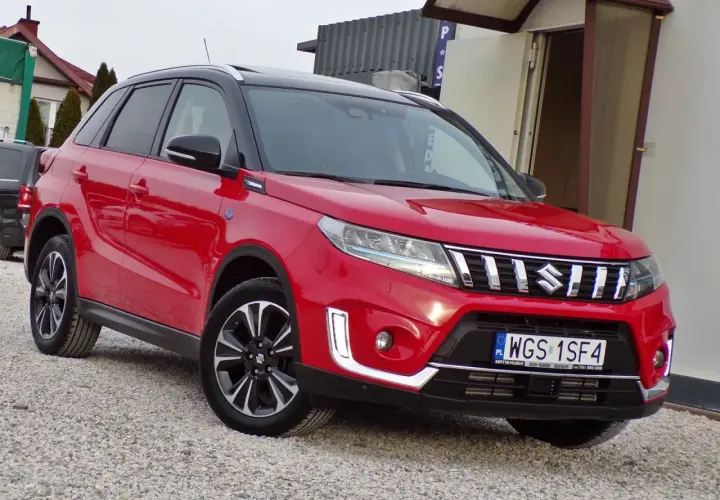 Czerwony Suzuki Vitara Hybrid z czarnym dachem, zaparkowany na żwirowej nawierzchni.