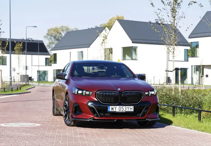 Czerwone bmw 550e na tle nowoczesnych domów.
