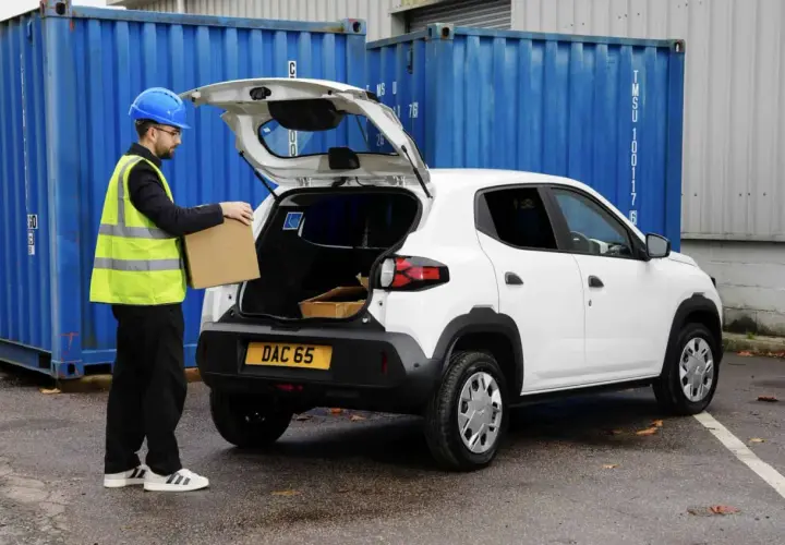 Pracownik w kamizelce odblaskowej wkłada paczkę do bagażnika białego Dacia Spring Cargo, gotowego do dostawy.