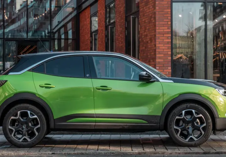Zielony Opel Mokka Electric z czarnym dachem stoi przed sklepem.