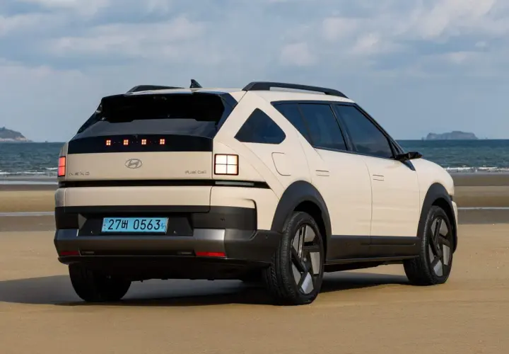 Kremowy Hyundai Nexo na plaży, z widokiem na morze i wyspę w oddali.