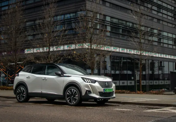 Biały Peugeot e-2008 zaparkowany przed nowoczesnym budynkiem.