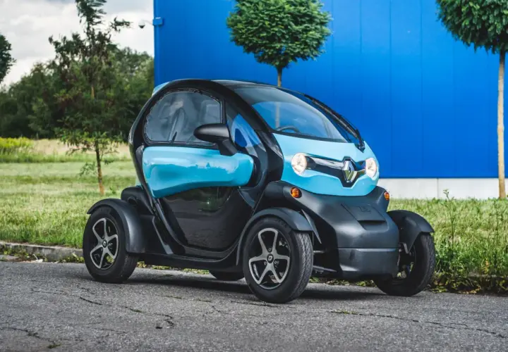 Niebiesko-czarny Renault Twizy stoi na drodze przed niebieskim budynkiem.