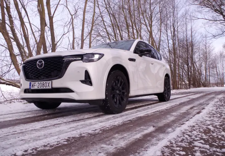 Biała Mazda hybryda na ośnieżonej drodze, otoczona zimowym lasem.