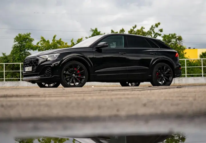 Czarny Audi Q9, lśniący po deszczu, z czerwonymi zaciskami hamulcowymi. Zastanawiasz się nad audi q9 cena?