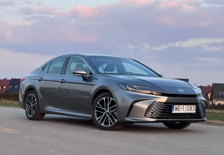 Szary Toyota Camry 2.5 Hybrid na tle zachodzącego słońca i domów.