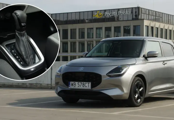 Srebrny Suzuki Swift Hybrid na parkingu przed budynkiem Poczty Polskiej. Widoczny detal dźwigni zmiany biegów.