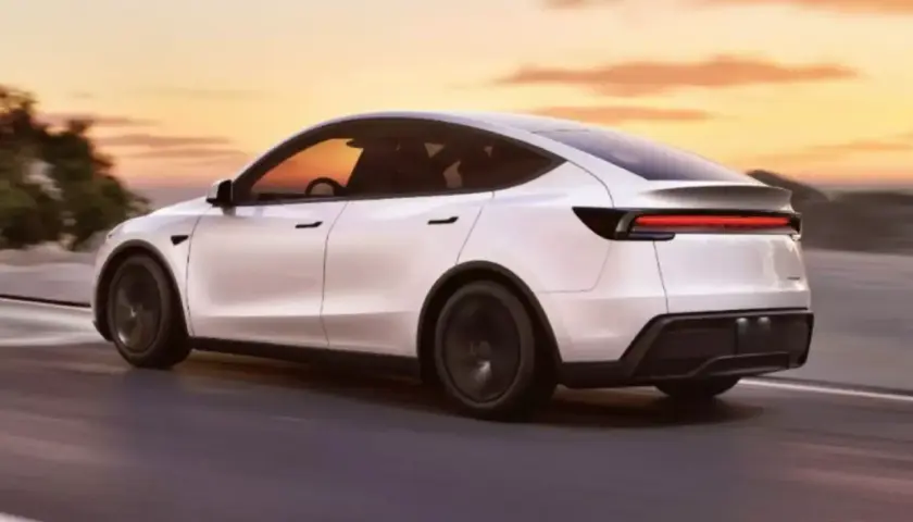 Biały Tesla Y 2025 pędzi po drodze o zachodzie słońca.