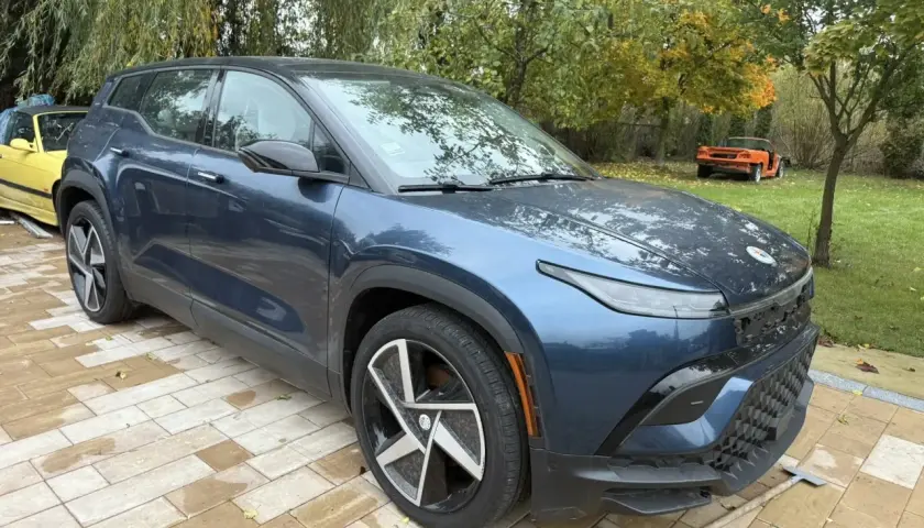Nowy, granatowy Fisker SUV stoi na wybrukowanym podjeździe. W tle żółty i pomarańczowy samochód.