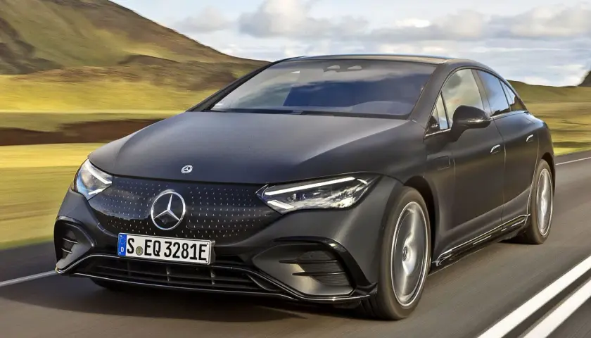 Elegancki, czarny Mercedes EQE sunie po drodze wśród malowniczych wzgórz.