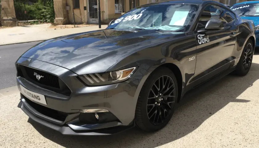 Szary Ford Mustang GT 5.0 z ceną 38 900 na szybie, gotowy do jazdy.