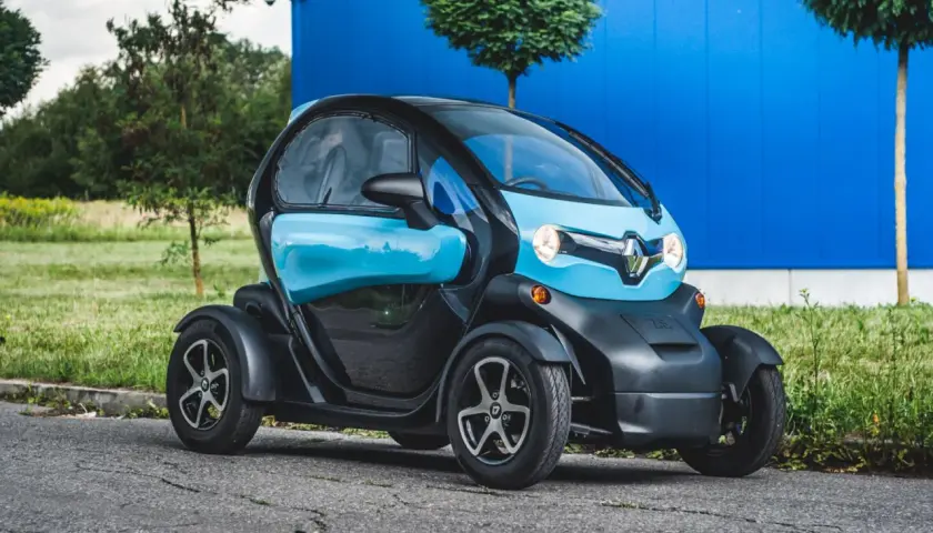 Niebiesko-czarny Renault Twizy stoi na drodze przed niebieskim budynkiem.
